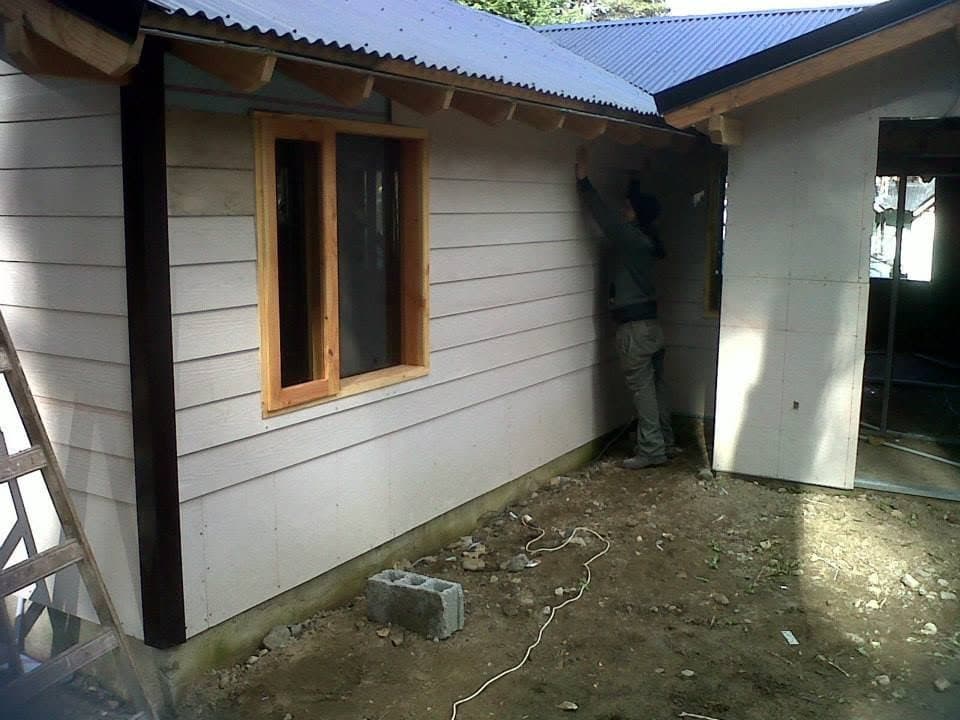 Casa blanca con techo a dos aguas y aberturas de madera, construcción en seco