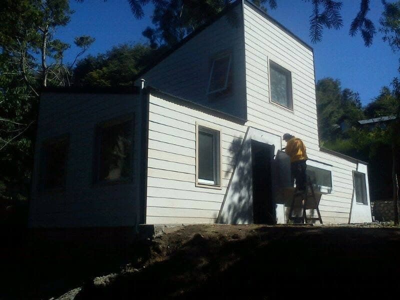 Casa de dos plantas con siding oscuro construida en seco en el bosque